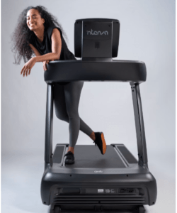 YOUNG GIRL MODEL LEANING ON A TREADMILL IN A PHOTO SHOOT. SHE WEARS A BLACK STRETCH SUIT WITH RUNNING SHOES