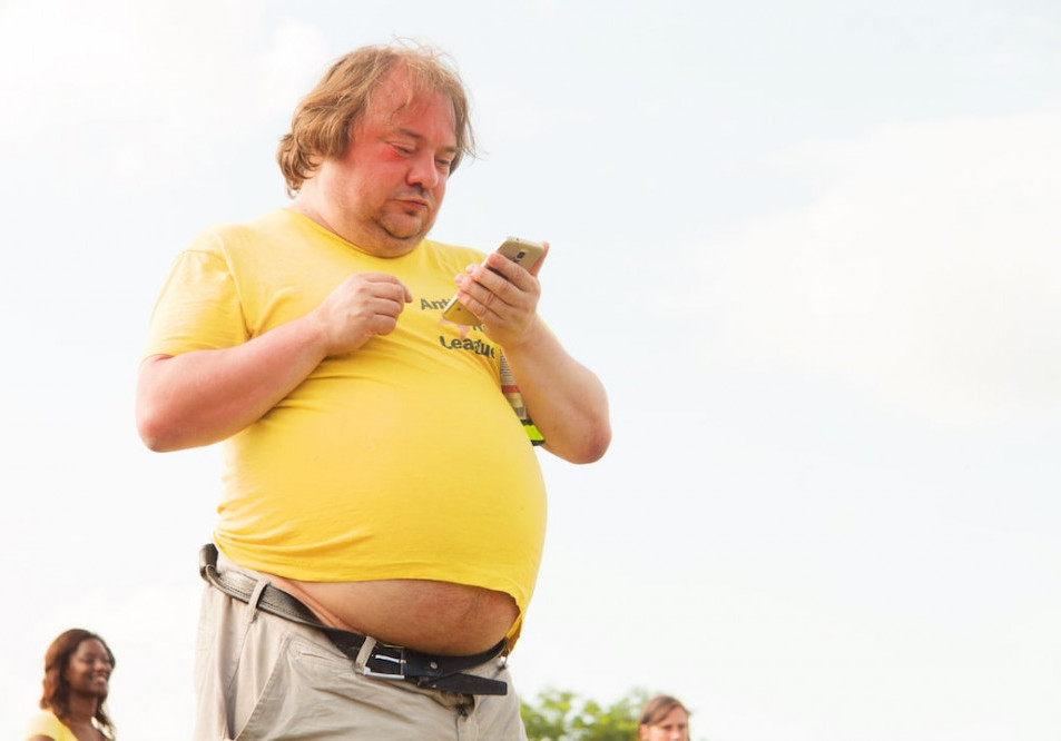 HOW HORMONAL CHANGES AFFECT WEIGHT LOSS - A CAUCASIAN MIDDLE-AGED MAN WITH LIGHT BROWN HAIR IS STANDING. HE IS WEARING A YELLOW SHORT SLEEVED TOP AND KAKI PANTS WITH A BELT. HIS BELLY IS HANGING OUT.