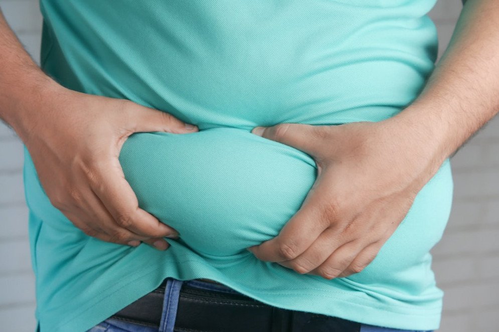 HOW HORMONAL CHANGES AFFECT WEIGHT LOSS - PERSON WEARING A SEA FOAM TOP IS GRABBING THE FAT AROUND HER BELLY