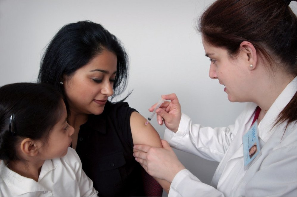 HOW HORMONAL CHANGES AFFECT WEIGHT LOSS - WOMEN WITH BLACK HAIR RECEIVING A SHOT FROM HER DOCTOR. HER LITTLE CHILD WATCHING AS SHE GETS THE INJECTION.