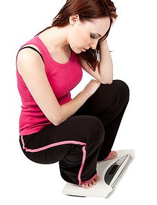 HOW TO WEAR MAGNETIC EARRINGS FR WEIGHT -  A YOUNG WOMAN QUATTING ON TOP OF A SCALE - WEARING A RED TANK TOP AND BLACK SWEAT PANTS WITH PINK STRIP DOWN THE SIDES