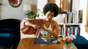 LADY WITH AN Afro, wearing a tan sweater-type top over a white tank top preparing a healthy meal in her doning room.