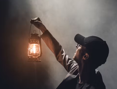 MAN WEARING A BLACK CAP ANS LON SLEEVE GRAY JACKET IS HOLDING UP A GASLIGHT