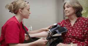 PATIENT GETTING HER BLOOD PRESSURE CHECKED BY PROVIDER WEARING RED SCRUBS