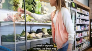 YOUNG BLONDE FEMALE SHOPPER WEARING A LONG SLEEVE WHITE SWEATER UNDER A SLEEVELESS PINK VESTIS SELECTING HER PRODUCE IN A GROCERY STORE