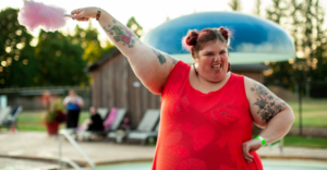 GIRL IN RED SLEEVELESS DRES HOLDING UP HER PINK COTTON CANDY AS SHE SMILES. SHE IS MORBIDLY OBESE