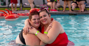 TWO FRIENDS HUGGING IAND SMILING N A POOL THAT MAY HAVE MORBID OBESITY