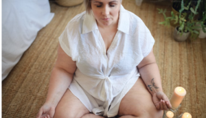 WOMAN IN WHITE COTTON SHORT SLEEVE OUTFIT WITH TIE BELT DOING MEDITATION AS SHE EMBARKS ON HER WEIGHT LOSS JOURNEY