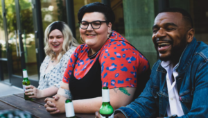 YOUNG WOMEN WEARING A BLACK SPAGETTI TOP WITH A RED AND BLE PRINT SHORT SLEEVE TOP WHO IS OBESE IS SMILING WITH HER FRIENDS 