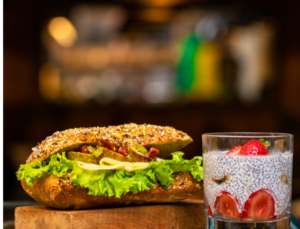 A HEALTHY LOOKING BAGETTE SANDWICH NEXT TO A CHIA PUDDING WITH STRAWBERRIES