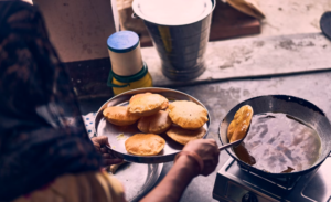 WOMEN IS FRYING HER ROUNDED BREADS ON A STOVE THE OLD-FASHIONED WAY