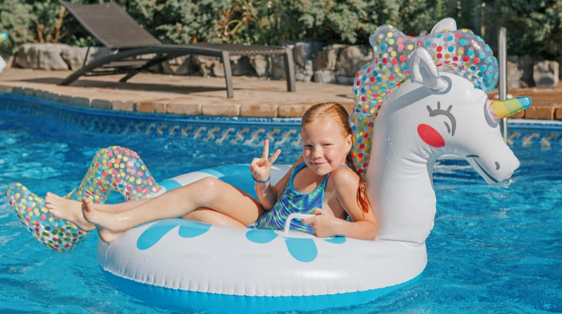 LITTLE GIRL ENJOYING SITTING IN A UNICORN RAFT GIVE US THE PEACE SIGN