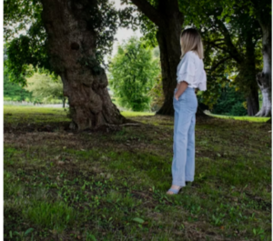 WOMEN WEARING A WHITE BLOUSE AND LIGHT BLUE JEANS THAT HAVE BEEN CARED FOR STANDING OUTDOORS NEAR TREES 