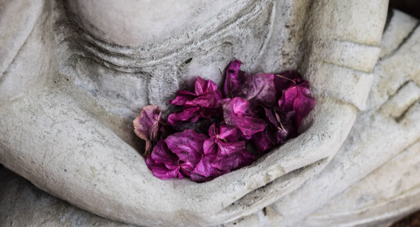 THE MIRACLE OF MINDFULNESS IN A WHITE STATUTE EMBRACING A BUNCH OF PURPLE FLOWER PETALS