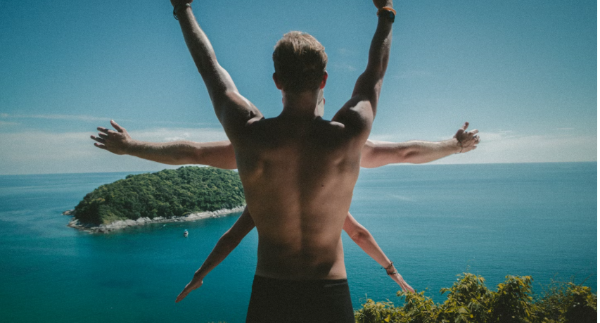 SHIRTLESS MAN WITH HIS BACK TO CAMERA WITH ARMS RAISED IN THE AIER WITH PEOPLE IN FRONT WITH THEIR ARMS SHOWIN OFF TO THE SIDES. LOOKS LIKE A 6-POINT START